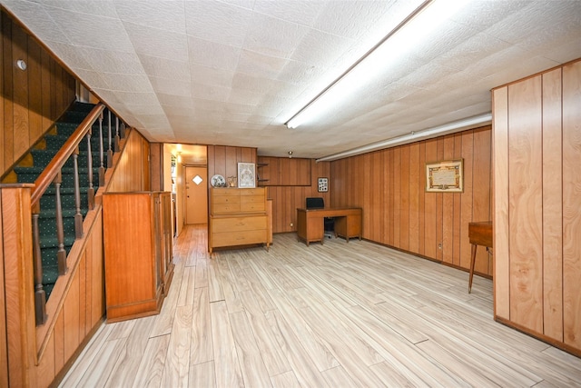 finished below grade area featuring light wood-style floors, wood walls, stairs, and baseboards
