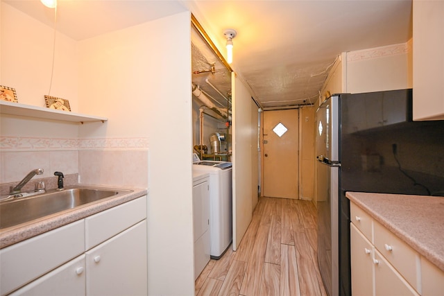 kitchen with washer and dryer, a sink, white cabinetry, and light countertops