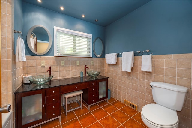 bathroom featuring tile walls, toilet, tile patterned floors, wainscoting, and double vanity