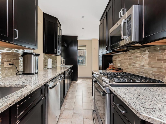 kitchen with appliances with stainless steel finishes, tasteful backsplash, dark cabinetry, light stone counters, and recessed lighting