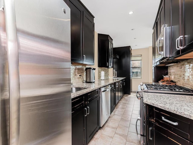 kitchen featuring stainless steel appliances, dark cabinets, decorative backsplash, light stone counters, and recessed lighting
