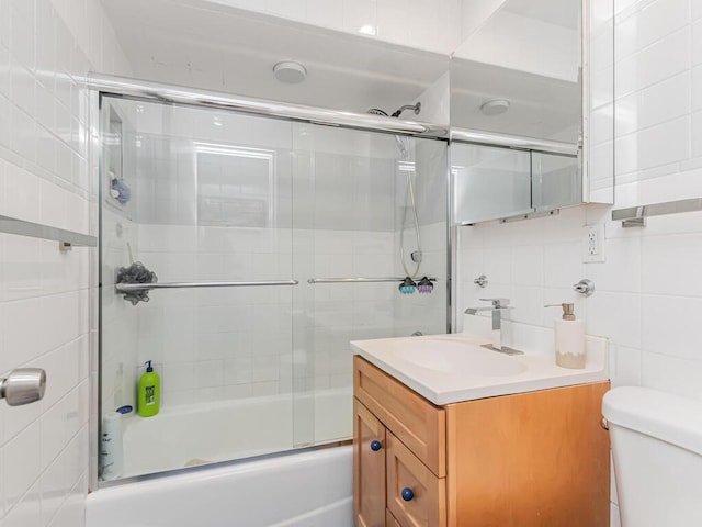 full bath with toilet, vanity, bath / shower combo with glass door, and tile walls