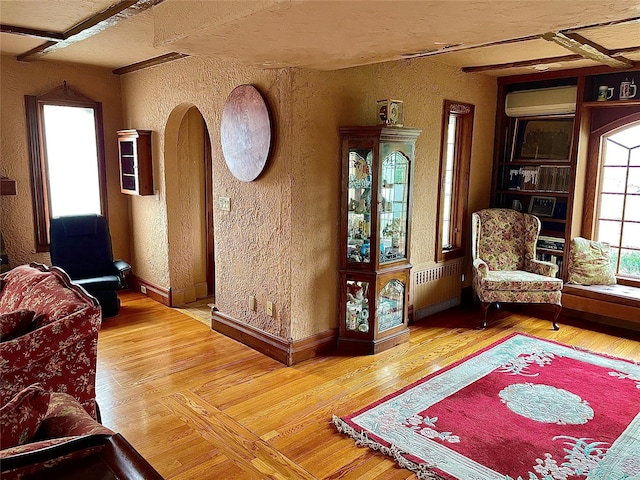 59 Sunset Rd, Bay Shore, NY 11706 - living area with a textured wall, radiator heating unit, an AC wall unit, wood finished floors, and baseboards