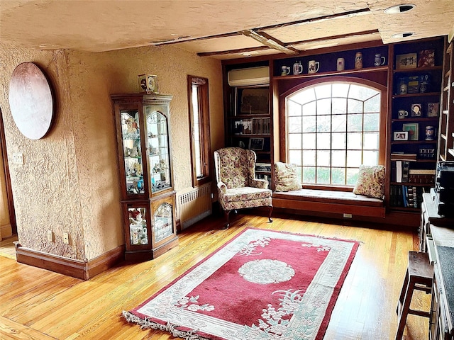 59 Sunset Rd, Bay Shore, NY 11706 - living area with radiator heating unit, a textured wall, a wall mounted air conditioner, wood-type flooring, and baseboards