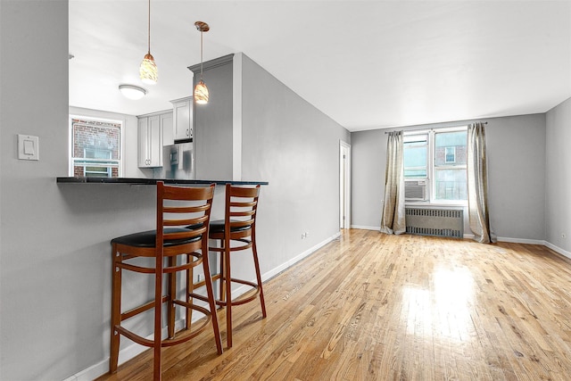 67-30 Clyde St Unit 6W, Forest Hills, NY 11375 - kitchen featuring radiator, wood finished floors, a breakfast bar, baseboards, and decorative light fixtures