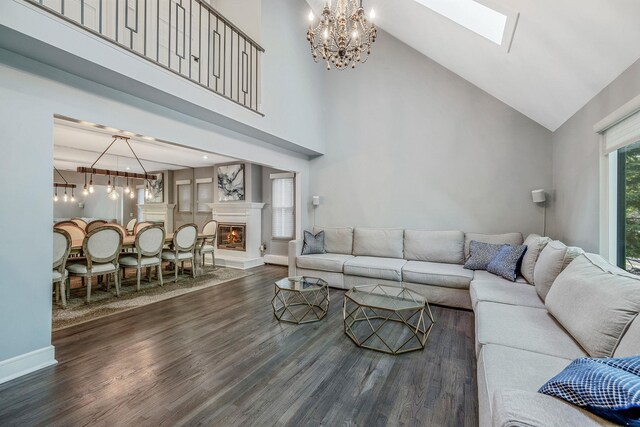 living area featuring a chandelier, high vaulted ceiling, dark wood-style floors, a skylight, and a glass covered fireplace