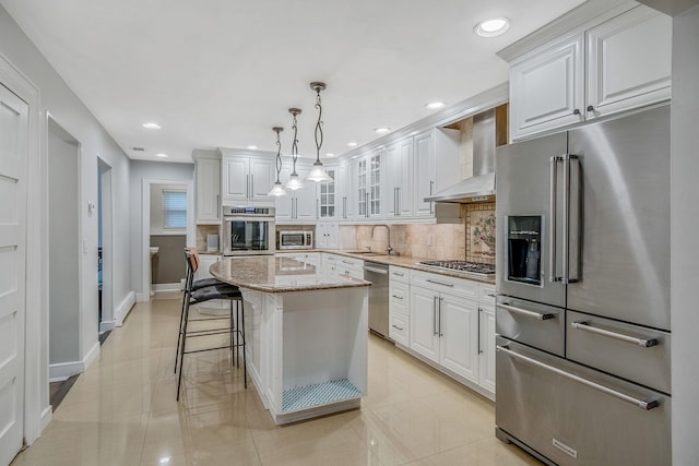 kitchen with stainless steel appliances, wall chimney range hood, a sink, tasteful backsplash, and white cabinets