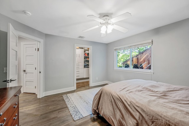 bedroom featuring baseboards, wood finished floors, a spacious closet, a ceiling fan, and a closet