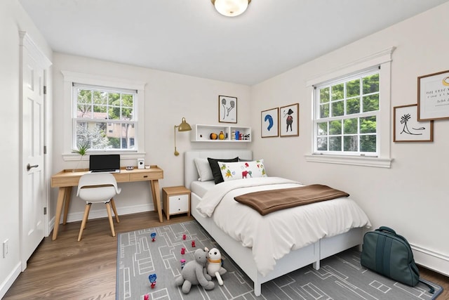 bedroom featuring wood finished floors, a desk, baseboards, and a baseboard heating unit