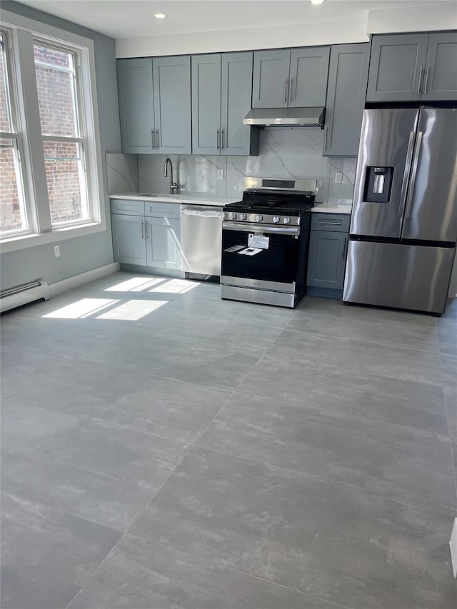 kitchen featuring appliances with stainless steel finishes, under cabinet range hood, a baseboard radiator, tasteful backsplash, and light countertops