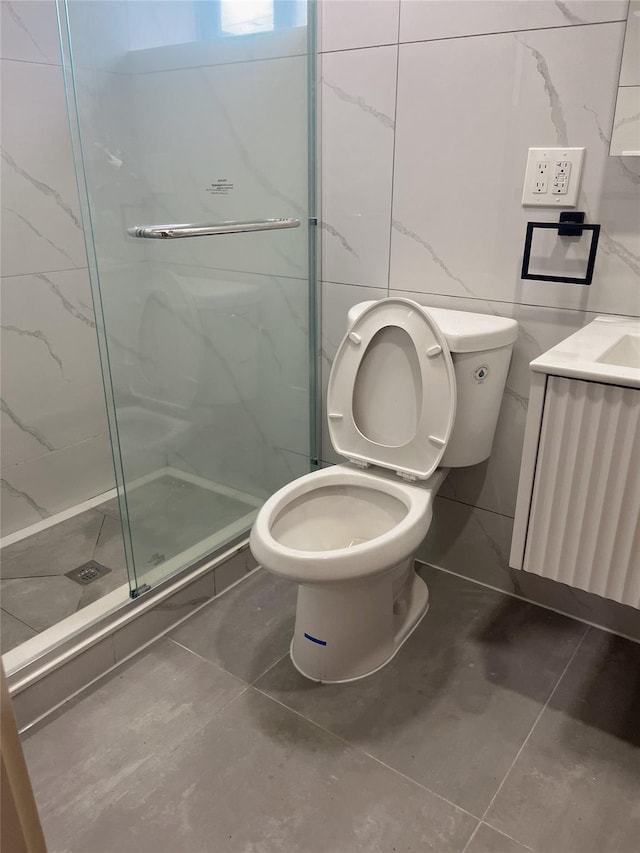 bathroom featuring tile walls, a marble finish shower, tile patterned floors, toilet, and vanity