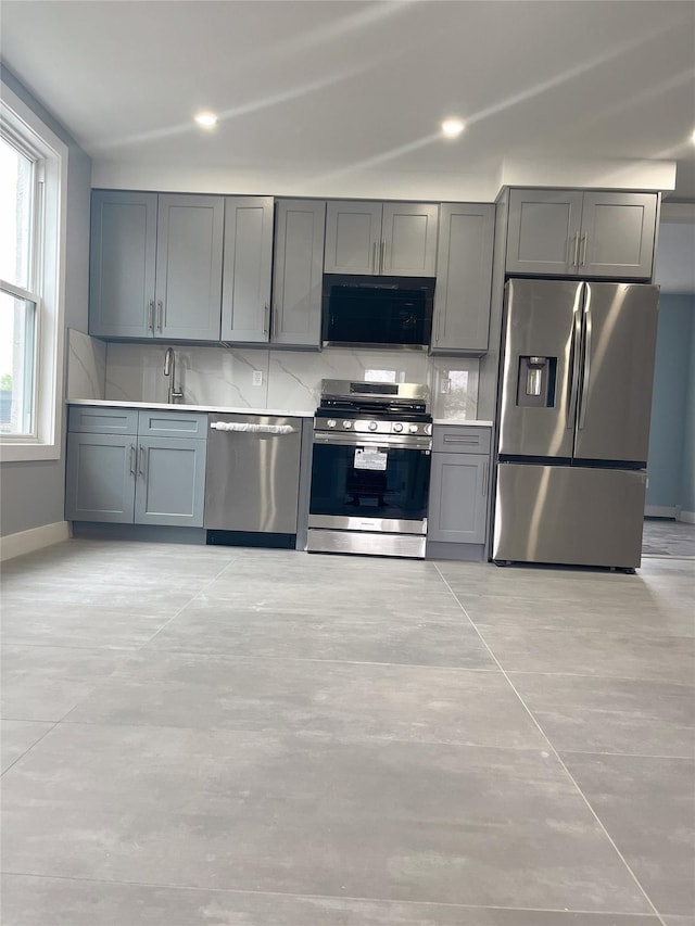 kitchen featuring appliances with stainless steel finishes, gray cabinetry, a sink, baseboards, and light countertops