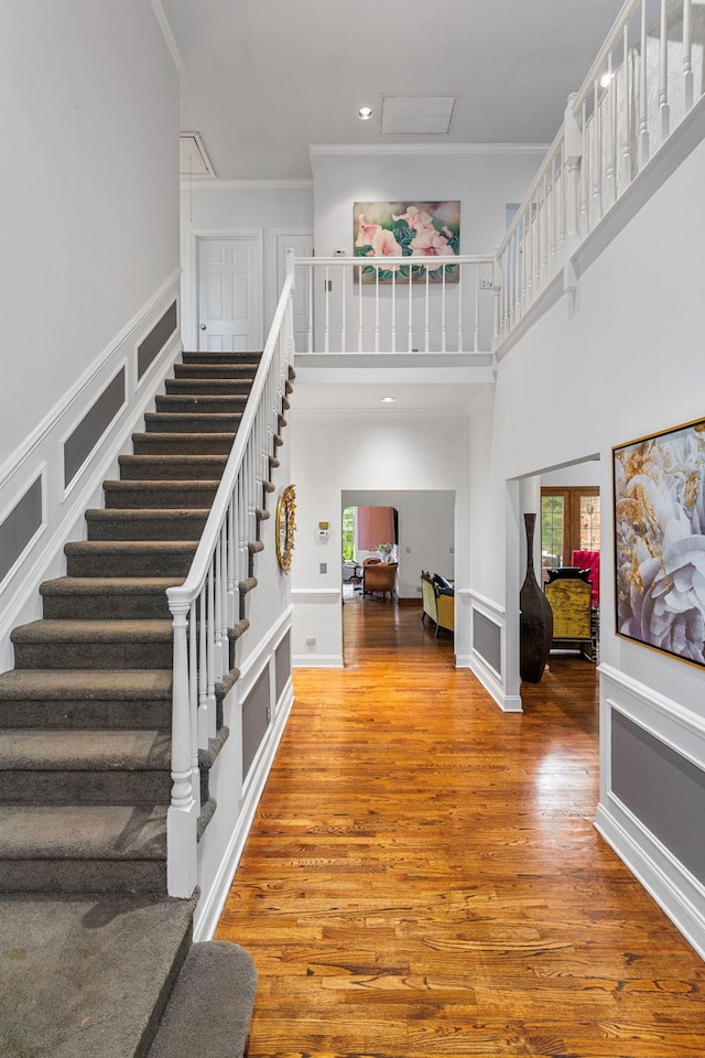 stairway featuring a towering ceiling, wood finished floors, crown molding, and recessed lighting