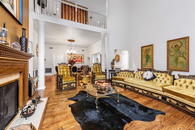 living room with ornate columns, a high ceiling, wood finished floors, and a chandelier