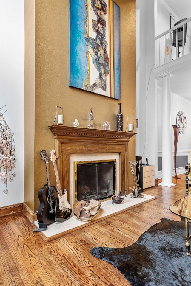 living area featuring a glass covered fireplace, wood finished floors, decorative columns, ornamental molding, and baseboards