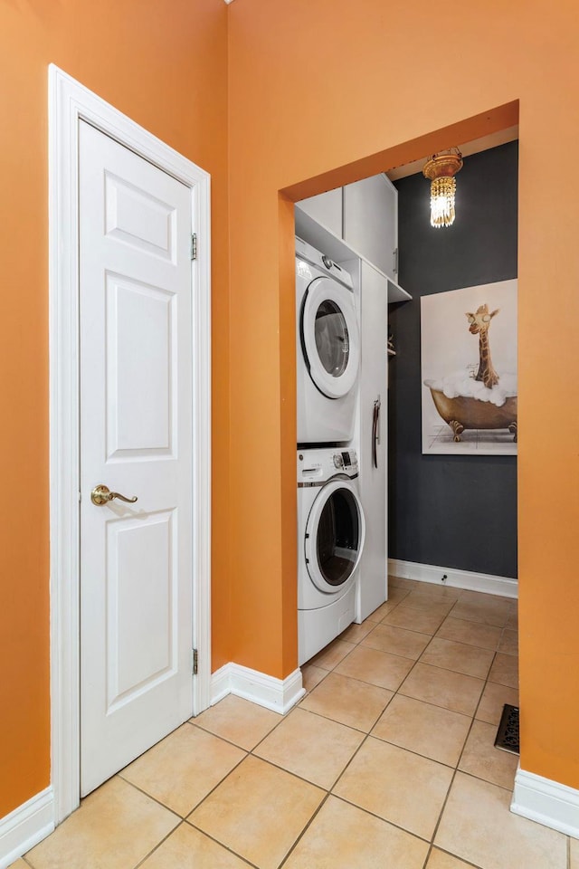 clothes washing area featuring stacked washer / drying machine, light tile patterned floors, baseboards, and a chandelier