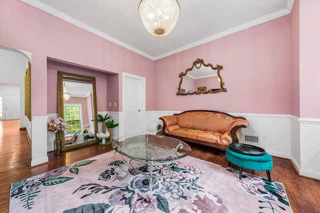 living area with wood finished floors, crown molding, arched walkways, and a wainscoted wall
