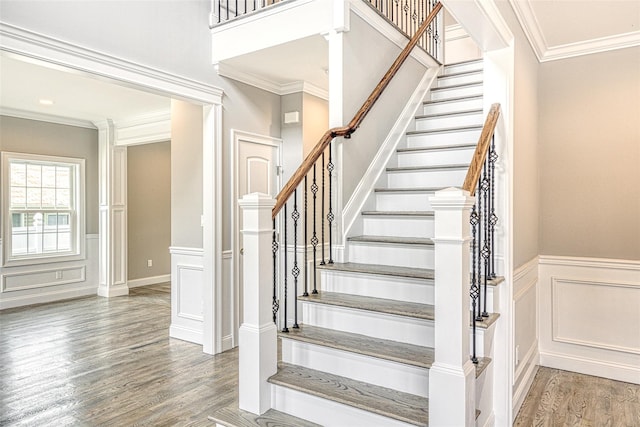 staircase featuring wood finished floors, ornamental molding, a decorative wall, and wainscoting