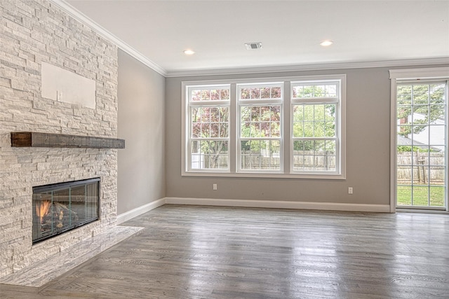 unfurnished living room with ornamental molding, baseboards, plenty of natural light, a stone fireplace, and wood finished floors