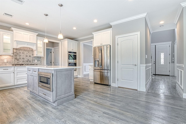 kitchen featuring stainless steel appliances, a decorative wall, crown molding, decorative backsplash, and light countertops