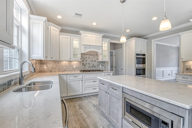 kitchen with a sink, ornamental molding, appliances with stainless steel finishes, white cabinets, and light wood finished floors