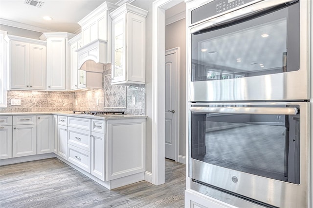 kitchen with stainless steel appliances, crown molding, light countertops, light wood-type flooring, and white cabinetry