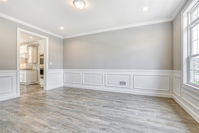 spare room featuring crown molding, a decorative wall, a wainscoted wall, light wood-style flooring, and recessed lighting