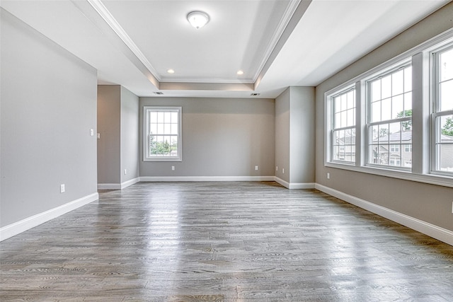 unfurnished room featuring a tray ceiling, wood finished floors, ornamental molding, baseboards, and recessed lighting