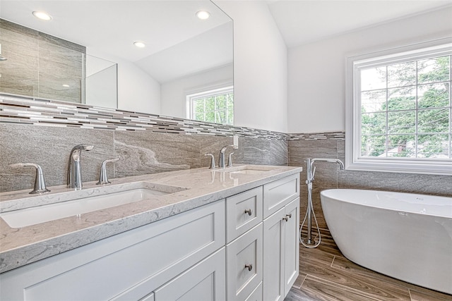 full bathroom featuring tile walls, double vanity, a freestanding tub, vaulted ceiling, and wood finished floors