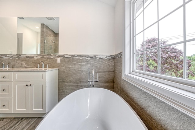 bathroom with tile walls, a freestanding bath, double vanity, a tile shower, and wood finished floors