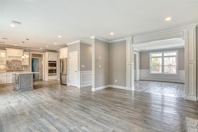 unfurnished living room featuring crown molding, wood finished floors, a decorative wall, recessed lighting, and a wainscoted wall