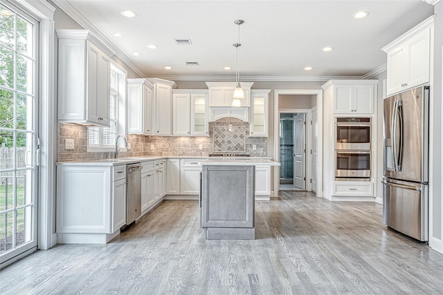 kitchen with stainless steel appliances, light wood finished floors, a sink, plenty of natural light, and ornamental molding