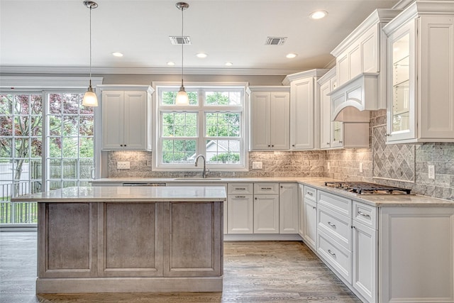 kitchen with a sink, stainless steel gas cooktop, light wood-style flooring, a kitchen island, and white cabinets