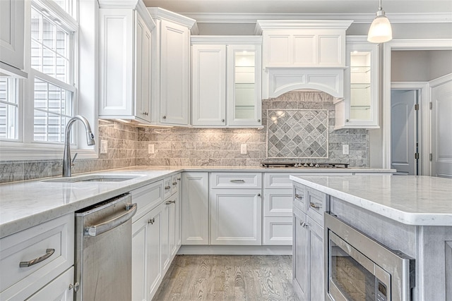 kitchen featuring appliances with stainless steel finishes, a sink, light wood-style flooring, white cabinets, and glass insert cabinets