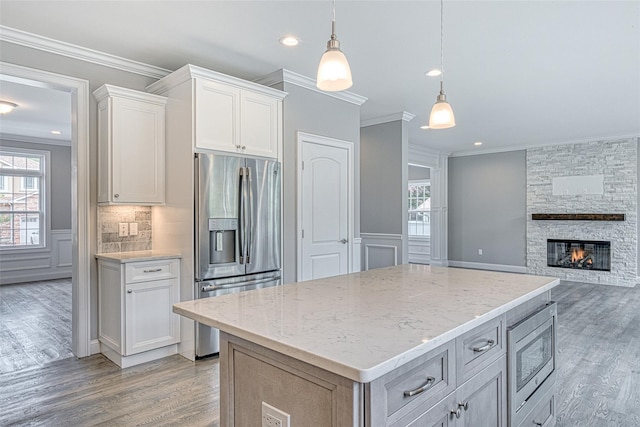 kitchen with stainless steel appliances, light wood-style flooring, ornamental molding, white cabinetry, and light stone countertops