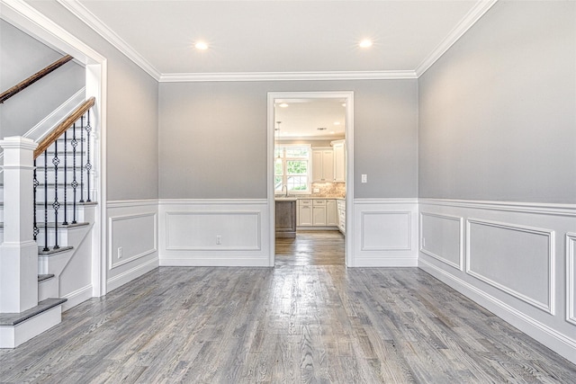 spare room featuring stairs, wood finished floors, wainscoting, a decorative wall, and crown molding