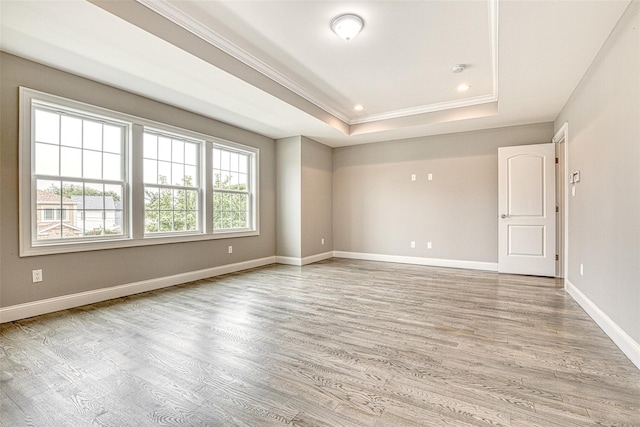 unfurnished room featuring a tray ceiling, light wood-style flooring, crown molding, baseboards, and recessed lighting