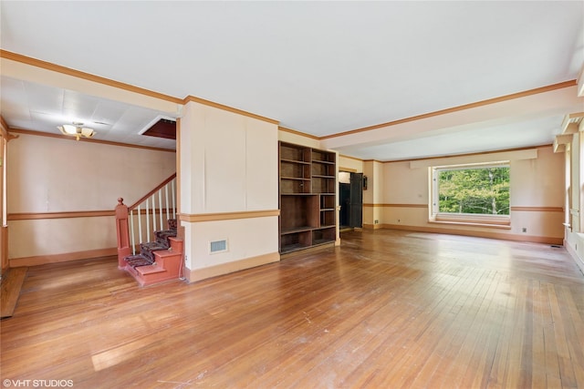 empty room featuring stairway, light wood-style floors, baseboards, and crown molding