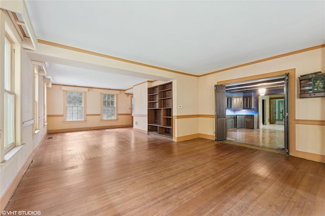 unfurnished living room with hardwood / wood-style flooring, crown molding, and baseboards
