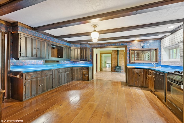 kitchen with a wood stove, light wood-style flooring, beam ceiling, range, and dishwasher