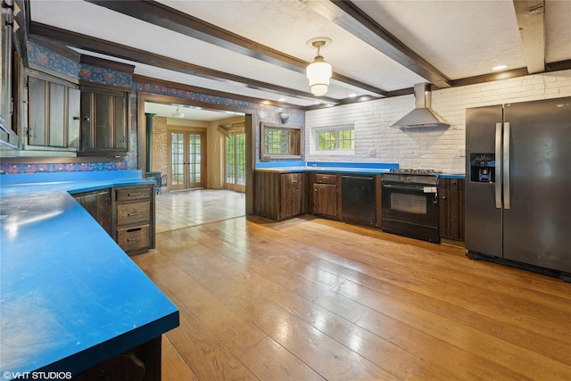 kitchen with black appliances, wall chimney range hood, light wood-style flooring, beamed ceiling, and dark brown cabinetry