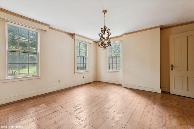 empty room with a chandelier, hardwood / wood-style floors, crown molding, and baseboards