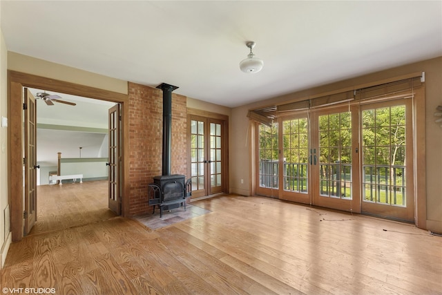 unfurnished living room featuring a wood stove, wood finished floors, french doors, and plenty of natural light