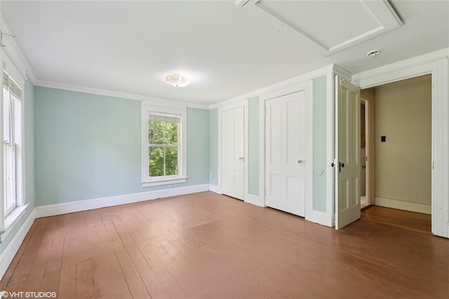 unfurnished bedroom with hardwood / wood-style flooring, multiple windows, multiple closets, and crown molding