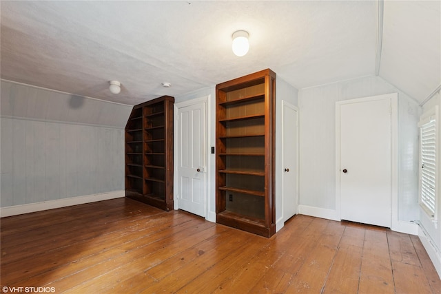 additional living space with wood-type flooring, built in shelves, lofted ceiling, baseboards, and wood walls