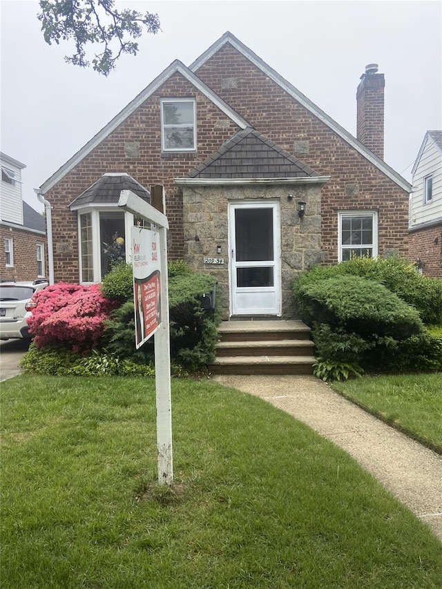 view of front of house featuring a chimney, a front yard, stone siding, and brick siding