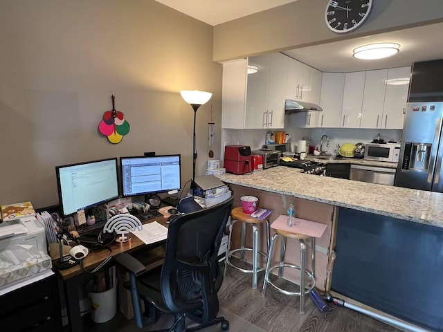 kitchen featuring stainless steel appliances, white cabinetry, a kitchen bar, an office area, and dark wood-type flooring