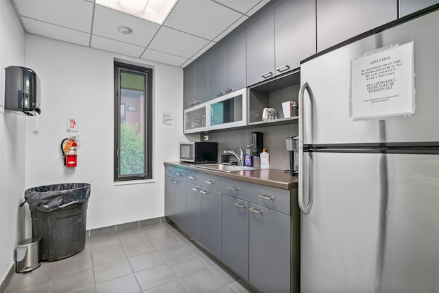 kitchen featuring stainless steel appliances, a sink, light tile patterned floors, gray cabinetry, and open shelves