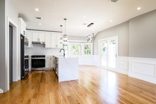 kitchen featuring under cabinet range hood, a peninsula, a sink, light stone countertops, and white cabinets