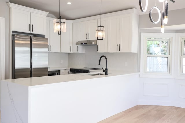 kitchen with freestanding refrigerator, a sink, a chandelier, white cabinetry, and under cabinet range hood